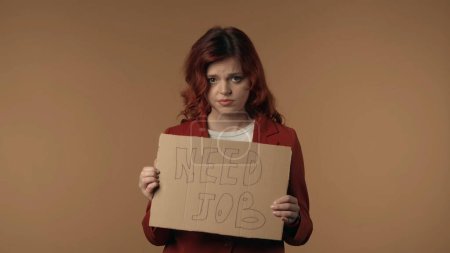 Photo for Medium isolated shot of a sad, tearful and pity young woman holding a piece of cardboard that says need job in her hands. Woman is looking from behind it. Job, vacancy offer or advertisement. - Royalty Free Image