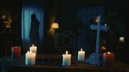 Téléchargez les photos : Prise de vue d'une table avec des outils magiques : bougies, croix et perles. Sur le fond, il y a une silhouette féminine floue, fantôme debout devant la fenêtre. Contenu créatif. - en image libre de droit