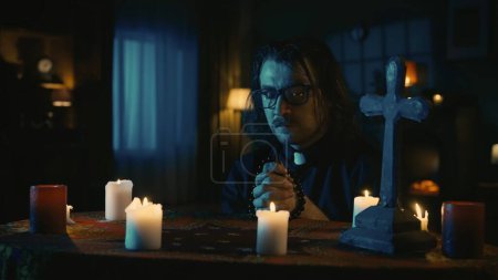Photo for Shot capturing a table with magical tools on it. A priest is sitting at the table with beads in his hands, praying with his eyes closed. Creative content, halloween themed. - Royalty Free Image