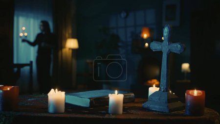 Téléchargez les photos : Prise de vue d'une table avec des outils magiques : bougies, croix et perles. Un prêtre avec un chandelier se tient près de la fenêtre. Place pour les rites et rituels occultes. Contenu créatif, thème Halloween. - en image libre de droit