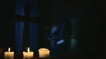 Photo for Shot capturring a blurry possessed female, ghost, entity with a knife in her hand, hunched over and shaking. On the foreground there are candles and a cross. Creative content, halloween themed. - Royalty Free Image