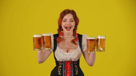 Photo for Medium yellow background isolated shot of a young German woman, waitress, wearing a traditional costume, holding four glasses of lager, beer, showing wow and excitement. Octoberfest, advertisement. - Royalty Free Image