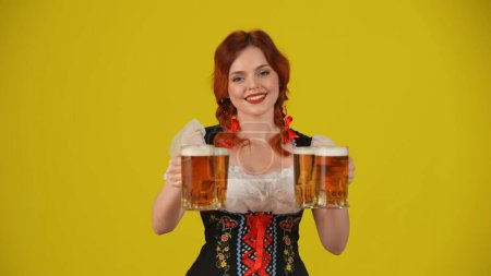 Photo for Medium yellow background isolated shot of a young German woman, waitress, wearing a traditional costume, holding a glass of lager, beer and smiling. Octoberfest, beer festival, advertisement. - Royalty Free Image