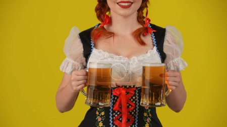 Photo for Close up yellow background isolated shot of an unrecognizable young German woman, waitress wearing a traditional costume, holding two glasses of lager, beer. Octoberfest, breasts, festival, advert. - Royalty Free Image