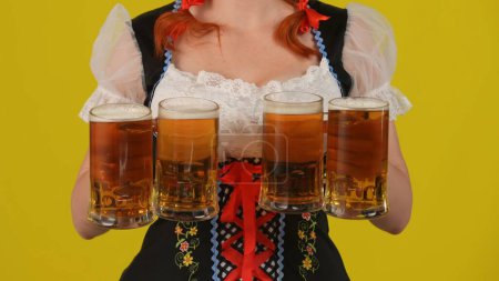 Photo for Close up yellow background isolated shot of an unrecognizable young German woman, waitress wearing a traditional costume, holding four glasses of lager, beer. Octoberfest, breasts, festival, advert. - Royalty Free Image