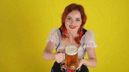 Photo for Medium yellow background isolated shot from above of a young German woman, waitress shot from above wearing a traditional costume, offering a glass of lager, beer. Octoberfest, advertisement. - Royalty Free Image