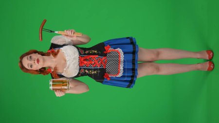 Foto de Pantalla verde vertical de tamaño completo con croma aislado de una joven alemana, camarera sosteniendo una urticaria, salchicha y un vaso de cerveza. Wow y emoción. Festival de octubre, festival de la cerveza, publicidad. - Imagen libre de derechos