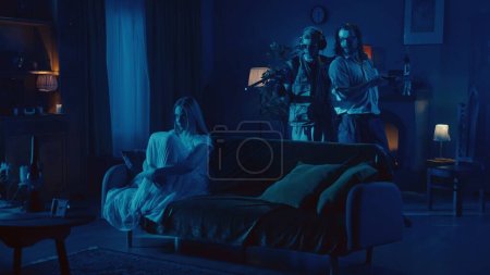 Vídeo de dos cazadores de fantasmas con un smartphone y un detector buscando signos de actividad paranormal, cuando ven a una mujer poseída, fantasma, poltergeist sentado en el sofá justo al lado de ellos.