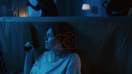 Photo for Shot of two burglars going around the dark apartment with flashlights on, as the owner, tenant is hiding behind the couch, sofa, calling the emergency hotline. Guard or security agency, advertisement. - Royalty Free Image