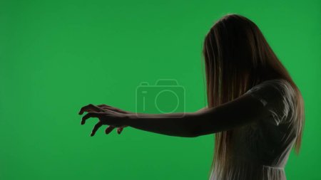 Foto de Pantalla verde de vista lateral media, captura de croma clave de una figura femenina poseída, fantasma, poltergeist, zombi sacando sus manos. El pelo le cubre la cara. Clip de terror, publicidad, muerto. Clave de croma. - Imagen libre de derechos