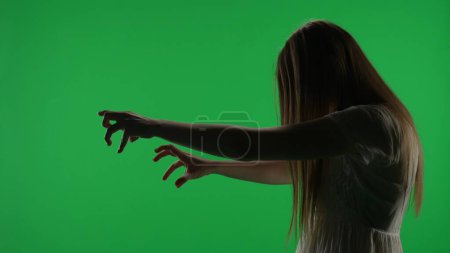 Photo for Medium side view green screen, chroma key shot of a posessed female figure, ghost, poltergeist, zombie pulling her hands out. Hair is covering her face. Horror clip, advertisement, dead. Chroma key. - Royalty Free Image