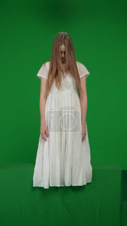 Photo for Full-size vertical green screen, chroma key shot of a posessed female, woman figure, ghost, poltergeist, zombie standing with her arms down, hunched. Horror clip, advertisement, dead. - Royalty Free Image