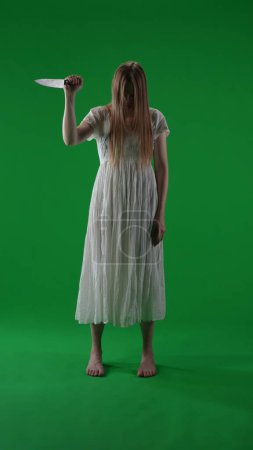 Photo for Full-size vertical green screen, chroma key shot of a posessed female, woman figure, ghost, poltergeist, zombie raising, pulling out a knife, stabbing the air. Horror clip, advertisement, walking dead - Royalty Free Image