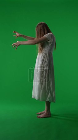 Photo for Full-size vertical side view green screen, chroma key shot of a posessed female figure, ghost, poltergeist, zombie pulling her hands out. Hair is covering her face. Horror clip, advertisement, dead. - Royalty Free Image