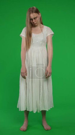 Photo for Full-size vertical green screen, chroma key shot of a posessed female, woman figure, ghost, poltergeist, zombie standing with her arms down, looking at the camera. Horror clip, advertisement, dead. - Royalty Free Image