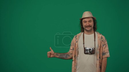 Photo for Travelling creative concept. Man in casual clothing and straw hat smiling looking at the camera and showing thumbs up. Space to insert advertising. Isolated on green background. - Royalty Free Image