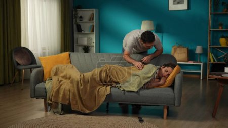 Photo for Full-size shot of a homosexual couple at home. One has just entered the room and saw their partner sleeping on the couch. He is leaning closer, fixing the blanket. LGBT, equality, educational, pride. - Royalty Free Image