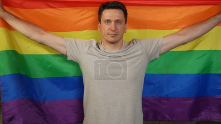 Photo for Medium shot of a homosexual, bisexual, pansexual, transgener person looking at the camera and holding LGBT flag to encourage love, equality, freedom. Educational content, pride, bravery. - Royalty Free Image