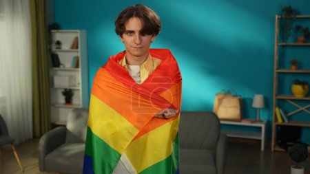 Téléchargez les photos : Plan moyen d'une personne homosexuelle, bisexuelle, pansexuelle, transgenre regardant la caméra et enveloppée dans un drapeau LGBT pour encourager l'amour, l'égalité, la liberté, la bravoure. Contenu éducatif, fierté. - en image libre de droit