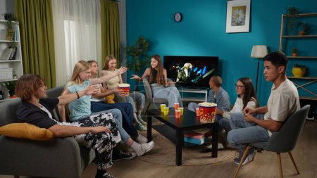 Photo for Group of teens, young people, friends sitting on a couch and watching TV, horror movie, series. They are eating popcorn and chatting, talking, joking around. Advertisement, teenage, youth content. - Royalty Free Image