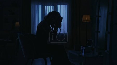 Photo for Portrait of a female model silhouette in the dark apartment. Everyday life creative concept. Closeup shot. Woman in a dress sitting on a chair in the room, brushing her hair with a brush. - Royalty Free Image