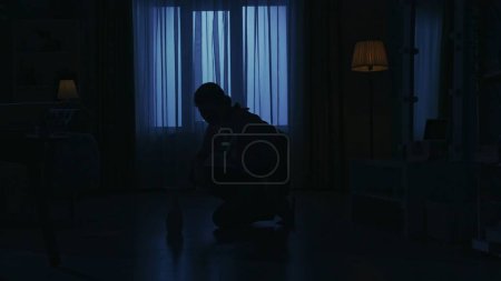 Photo for Portrait of female silhouette in the dark apartment room. Everyday life creative concept. Woman in casual clothing polishing the floor in the living room with a brush and cleanser. - Royalty Free Image