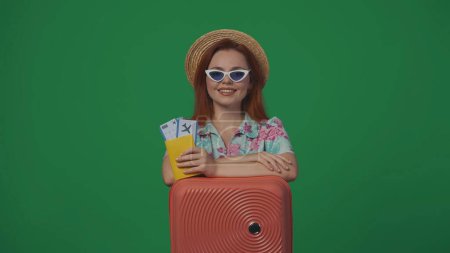 Foto de Concepto creativo de publicidad itinerante. Mujer viajera en sombrero de paja y gafas con maleta con billetes de avión, pasaporte y sonriente. Aislado sobre fondo verde. - Imagen libre de derechos