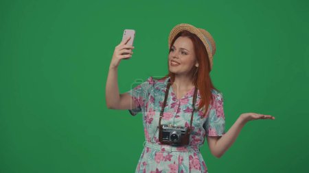 Téléchargez les photos : Publicité itinérante concept créatif. Femme voyageuse en chapeau parlant sur smartphone par un appel vidéo, souriant posant expression joyeuse visage. Isolé sur fond vert. - en image libre de droit