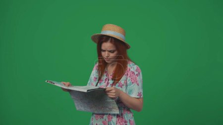 Photo for Travelling advertisement creative concept. Woman traveller in straw hat and dress holding paper map looking at it, finding right direction. Isolated on green background. - Royalty Free Image