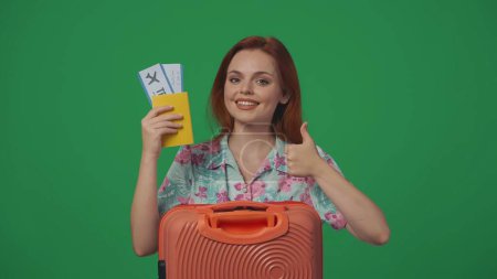 Photo for Travelling advertisement creative concept. Woman traveller holding flight tickets, shows thumbs up with happy smiling face expression. Isolated on green background. - Royalty Free Image