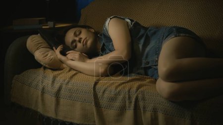 Horror movie scene. Halloween advertisement concept. Closeup shot of young girl in casual clothes calmly laying sleepping on the sofa in the dark living room.