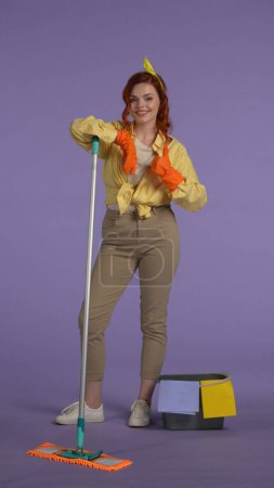 Photo for Everyday housekeeping creative concept. Vertical photo. Woman in casual clothing and rubber gloves with smiling face expression looking at the camera and showing thumbs up gesture. - Royalty Free Image