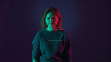 Photo for Portrait of an upset woman in a studio on a blue background in pink and green neon light close up - Royalty Free Image