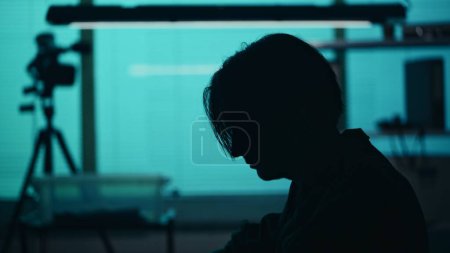 Photo for Close up silhouette shot of a suspect, offender, perpetrator or prisoner sitting in the interrogation room. He is looking down with remorse and frustration. True crime, documentary, creative content. - Royalty Free Image
