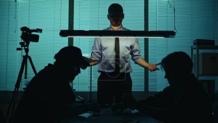 Silhouette, medium shot of a suspect, perpetrator, prisoner sitting in the interrogation room with detective and policeman. They try to get the confession. True crime, documentary, creative content.