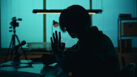 Photo for Medium silhouette shot of a suspect, offender, perpetrator or prisoner sitting in the interrogation room. He is waving at the camera. True crime, documentary, creative content. - Royalty Free Image