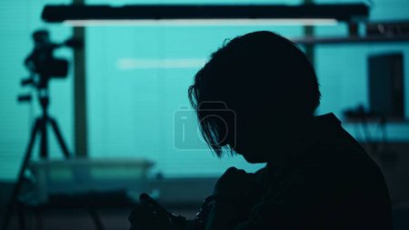 Photo for Close up silhouette shot of a suspect, offender, perpetrator or prisoner sitting in the interrogation room. He is looking down with remorse and frustration. True crime, documentary, creative content. - Royalty Free Image