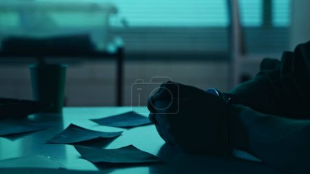 Photo for Close up detail shot of the hands of a suspect, offender, perpetrator or prisoner studying the evidence on the table in the interrogation room. True crime, documentary, creative content. - Royalty Free Image