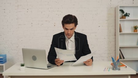 Foto de Vídeo mediano de un joven sentado en el escritorio de una oficina, chechando los gráficos y gráficos, investigándolos y analizándolos. Parece interesado y satisfecho. Analitics, anuncio de negocios. - Imagen libre de derechos