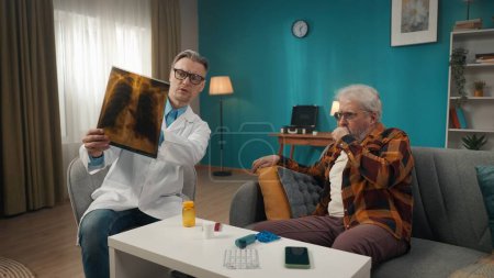 Photo for Full-size shot of a doctor checking up the condition of his patient at home. He is talking to an eldery man with health issues and checking an x-ray. Healthcare system, medical service, advertisement. - Royalty Free Image