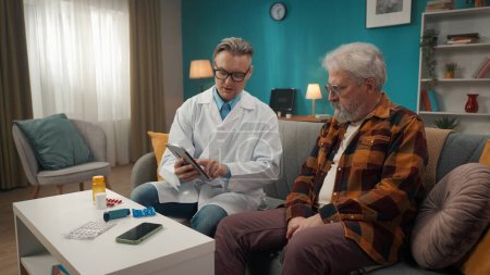 Photo for Full-size shot of a doctor checking up the condition of his patient at home. He is showing something on a tablet to an eldery man with health issues. Healthcare, medical service, advertisement. - Royalty Free Image