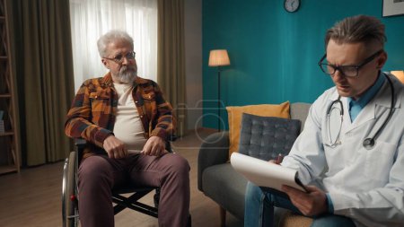 Photo for Full-size shot of a doctor checking up the condition of his patient at home. He is talking to an eldery man on a wheelchair, writing something down on a notepad. Healthcare, medical, advertisement. - Royalty Free Image