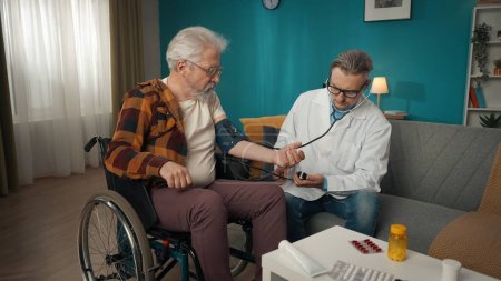 Photo for Full-size shot of a doctor checking up his patient at home. He is using stethoscope and a device for measuring blood pressure of an eldery man on a wheelchair. Medical service, advertisement. - Royalty Free Image