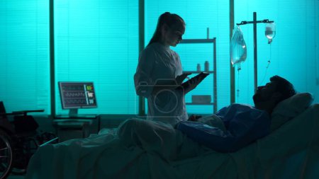 Photo for Full-sized silhouette shot of a double amputee patient laying in a hospital bed. A female doctor, nurse comes in for a check-up. She talks to a patient. Hostital, surgical treatment, disability. - Royalty Free Image