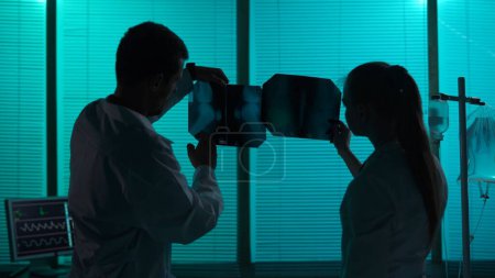 Téléchargez les photos : Silhouette de taille moyenne prise de vue de deux médecins debout dans une salle d'hôpital. Les médecins examinent les patients jambe, genou radiographie, discuter du diagnostic et une méthode de traitement. Hôpital, soins médicaux. - en image libre de droit
