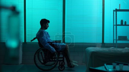 Foto de Foto de silueta de tamaño completo de un hombre discapacitado, paciente con discapacidad de movilidad que entra en el marco en una silla de ruedas, mirando a la ventana tristemente. Hospital, cambios drásticos, servicio médico. - Imagen libre de derechos