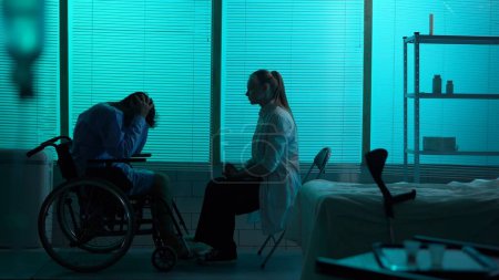 Photo for Full-sized silhouette shot a disabled man, patient with mobility impairment on a wheelchair talking to a female doctor who tells him bad news. The man is shocked and desperate. Hospital - Royalty Free Image