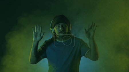 Photo for A man wearing wireless headphones dances while enjoying the music. A man dances in a studio in the beams of a spotlight, in clouds of smoke in multicolored neon light - Royalty Free Image
