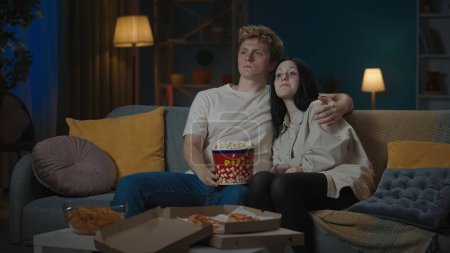 Photo for First relationships creative concept. Portrait of teenage couple spending leisure time. Boy and girl sitting on the sofa eating popcorn and watching movie and hugging. - Royalty Free Image