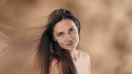Photo for In the frame is a middle-aged woman with long, dark hair. Turning slightly to the side, she looks at the camera and smiles. The wind is blowing on her developing the hair that covered her face. - Royalty Free Image